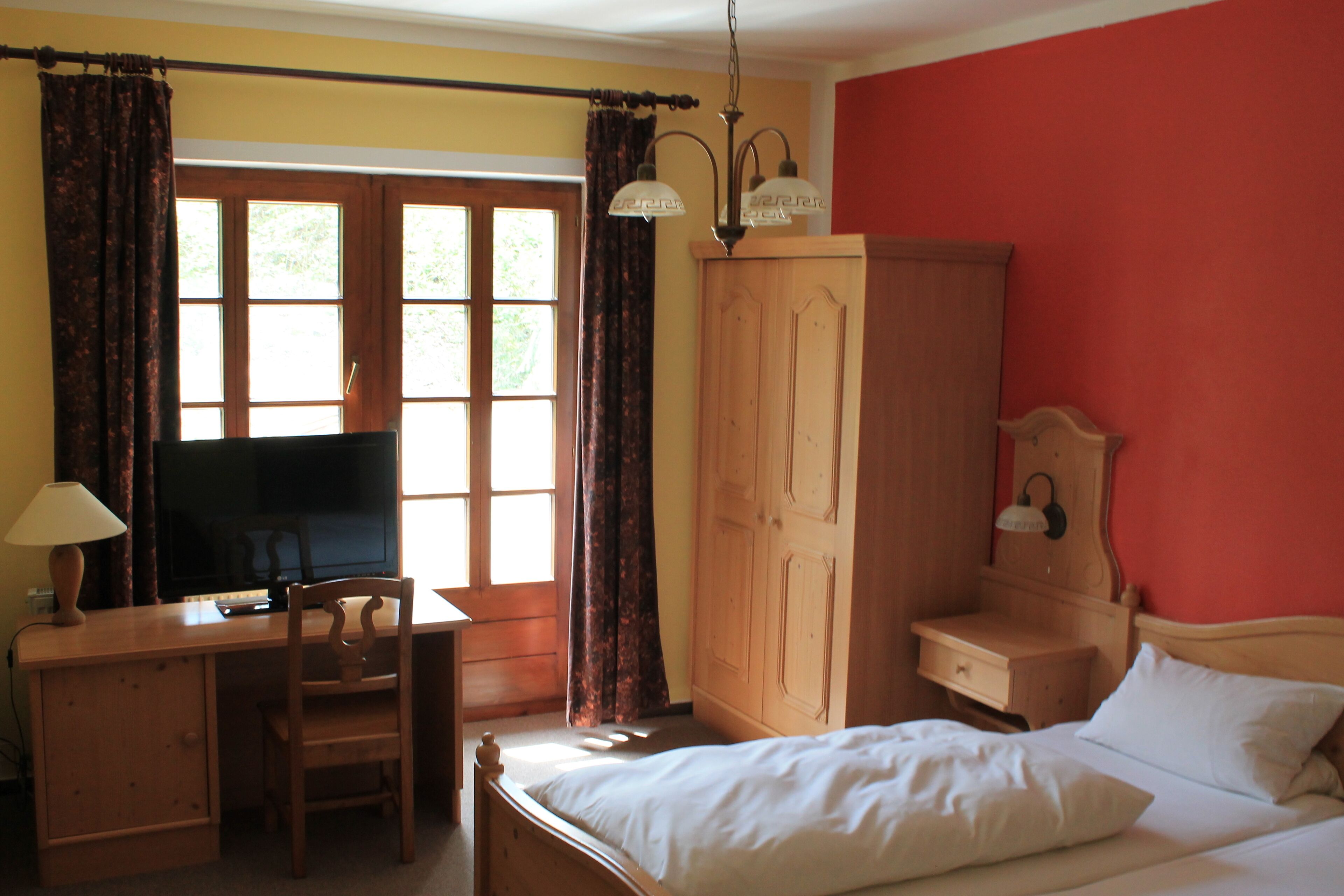 Une chambre avec un lit, un bureau avec une télévision, une armoire et une fenêtre avec des rideaux.