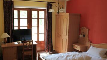 Une chambre avec un lit, un bureau avec une télévision, une armoire et une fenêtre avec des rideaux.