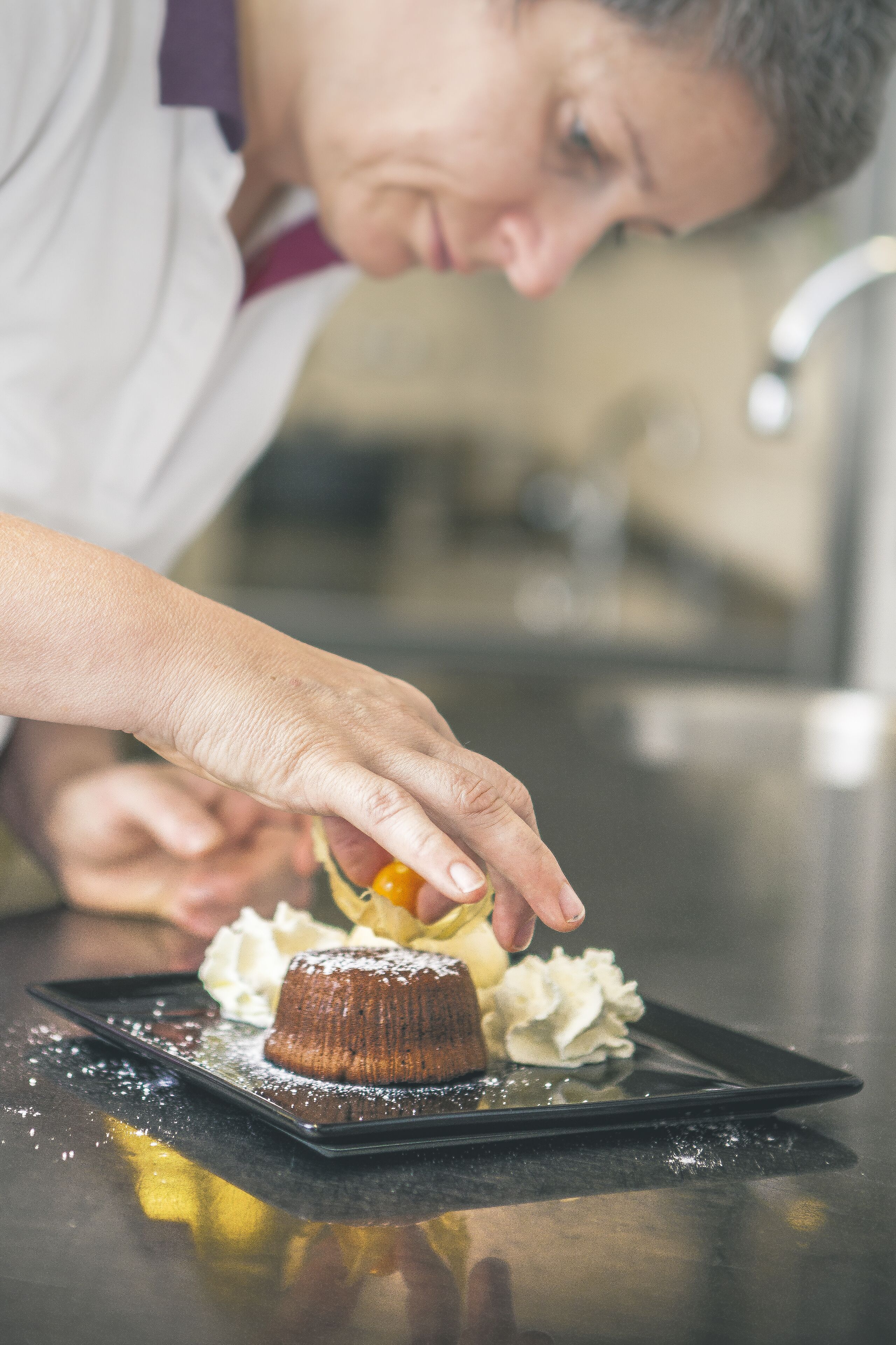 A chef preparing a dessert on a black plate with powdered sugar.