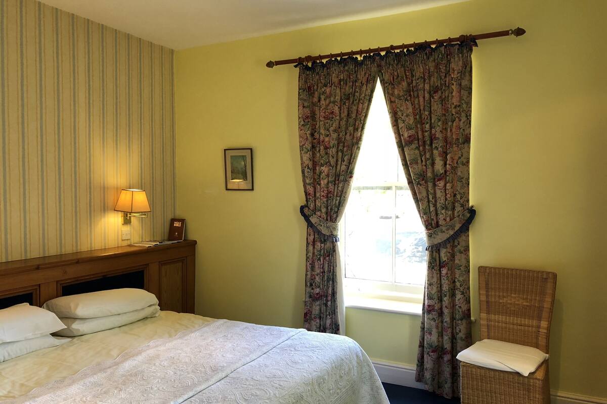 A hotel room with a bed, a chair, a lamp, and curtains.