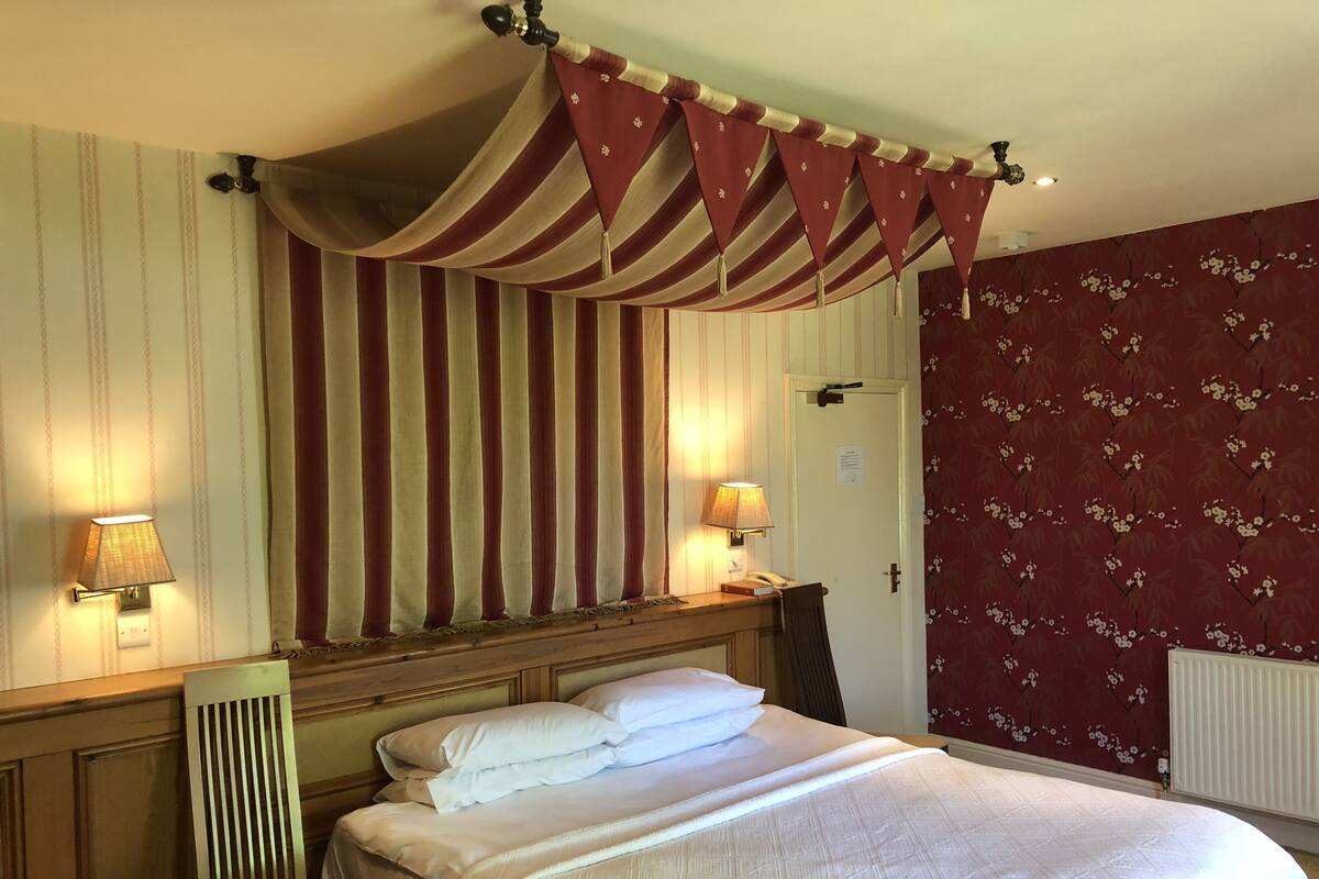 A hotel room with a large bed, two bedside lamps, a wooden headboard, a chair, and striped curtains.