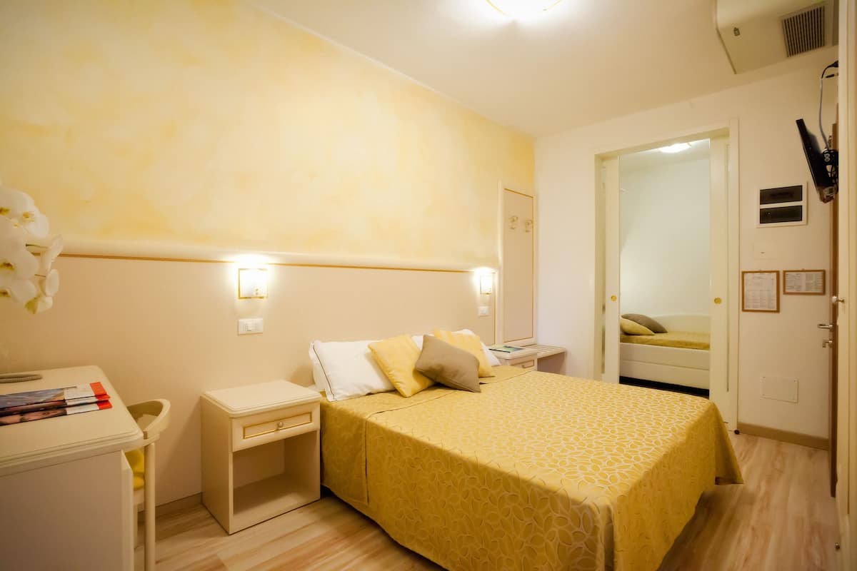 Una habitación de hotel con cama, mesitas de noche, escritorio y silla, y un espejo en la pared.
