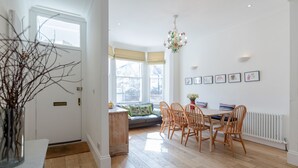 A bright, spacious room with a wooden floor, a dining table with chairs, a sofa with cushions, and a chandelier. - Vauxhall Oasis - 3 Bed House by BaseToGo (London)