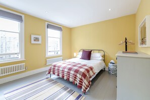 A bedroom with a bed, a bedside table, a radiator, a window, and a hanging clothes rack.