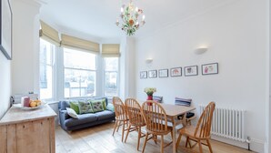 A bright living room with a sofa, wooden chairs, a dining table, and a chandelier. - Vauxhall Oasis - 3 Bed House by BaseToGo (London)