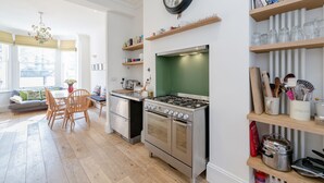 A modern kitchen with a stove, oven, and wooden dining table. - Vauxhall Oasis - 3 Bed House by BaseToGo (London)