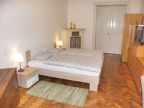 Une chambre à coucher avec un lit, des tables de chevet, une lampe, un tapis, une commode en bois et une porte.