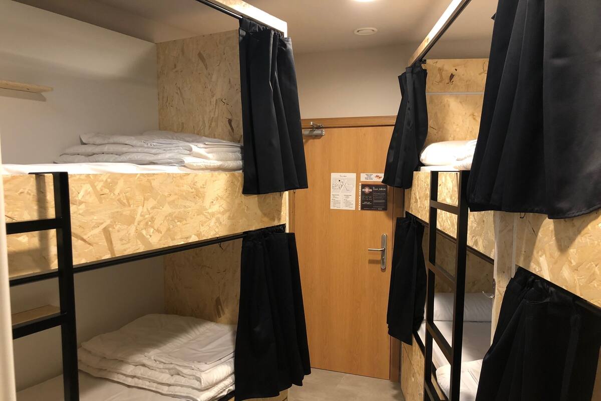Habitación con literas, paredes de madera, una puerta con un letrero y cortinas negras.