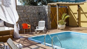 A pool area with a stone wall, wooden deck, and lounge chairs. - Apart Hotel Fênix (Florianópolis)