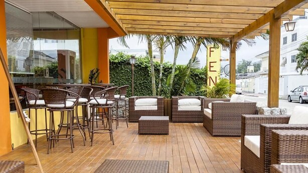 A covered outdoor seating area with wicker furniture and a wooden floor. - Apart Hotel Fênix (Florianópolis)