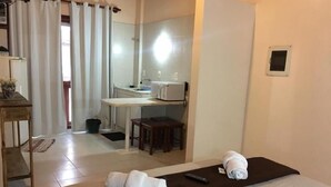 A hotel room with a bed, a desk, a chair, a small table, a mirror, a window with curtains, and a wall-mounted light. - Apart Hotel Fênix (Florianópolis)