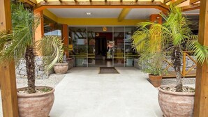 A hotel entrance with a tiled floor, large potted plants, and a welcome mat with 'FENIX' written on it. - Apart Hotel Fênix (Florianópolis)