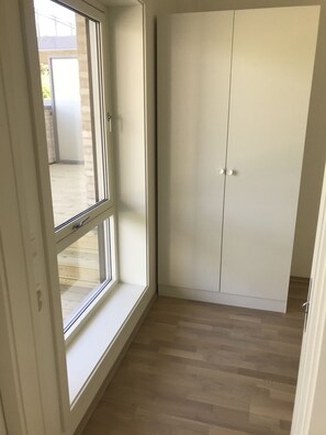 A room with a large window, wooden flooring, and a white wardrobe.