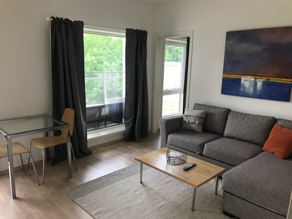 A living room with a glass table, two chairs, a sofa, a coffee table, and a painting on the wall.