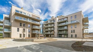 A modern multi-story residential building with balconies, a central courtyard, and a playground. - Fornebu Apartments - Fornebuporten (Bærum)
