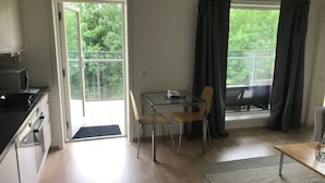A small kitchen with a microwave, a dining table with two chairs, and a view of greenery through the windows. - Fornebu Apartments - Fornebuporten (Bærum)