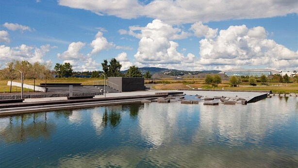 A tranquil outdoor pool area with a modern architectural structure, a clear sky, and distant hills. - Fornebu Apartments - Fornebuporten (Bærum)