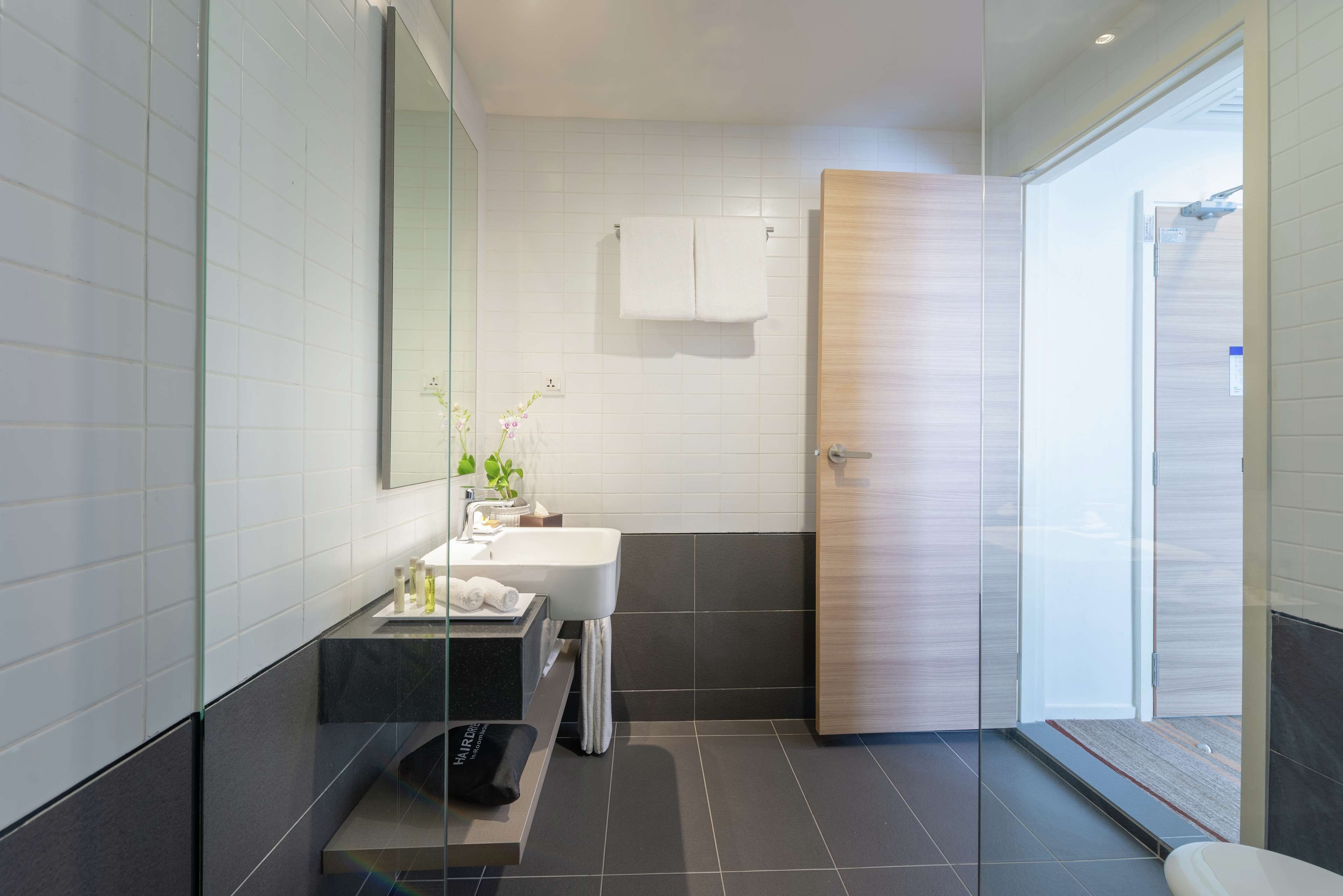 A modern bathroom with a glass shower enclosure, a white sink, and a wooden door.