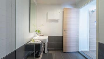 A modern bathroom with a glass shower enclosure, a white sink, and a wooden door.