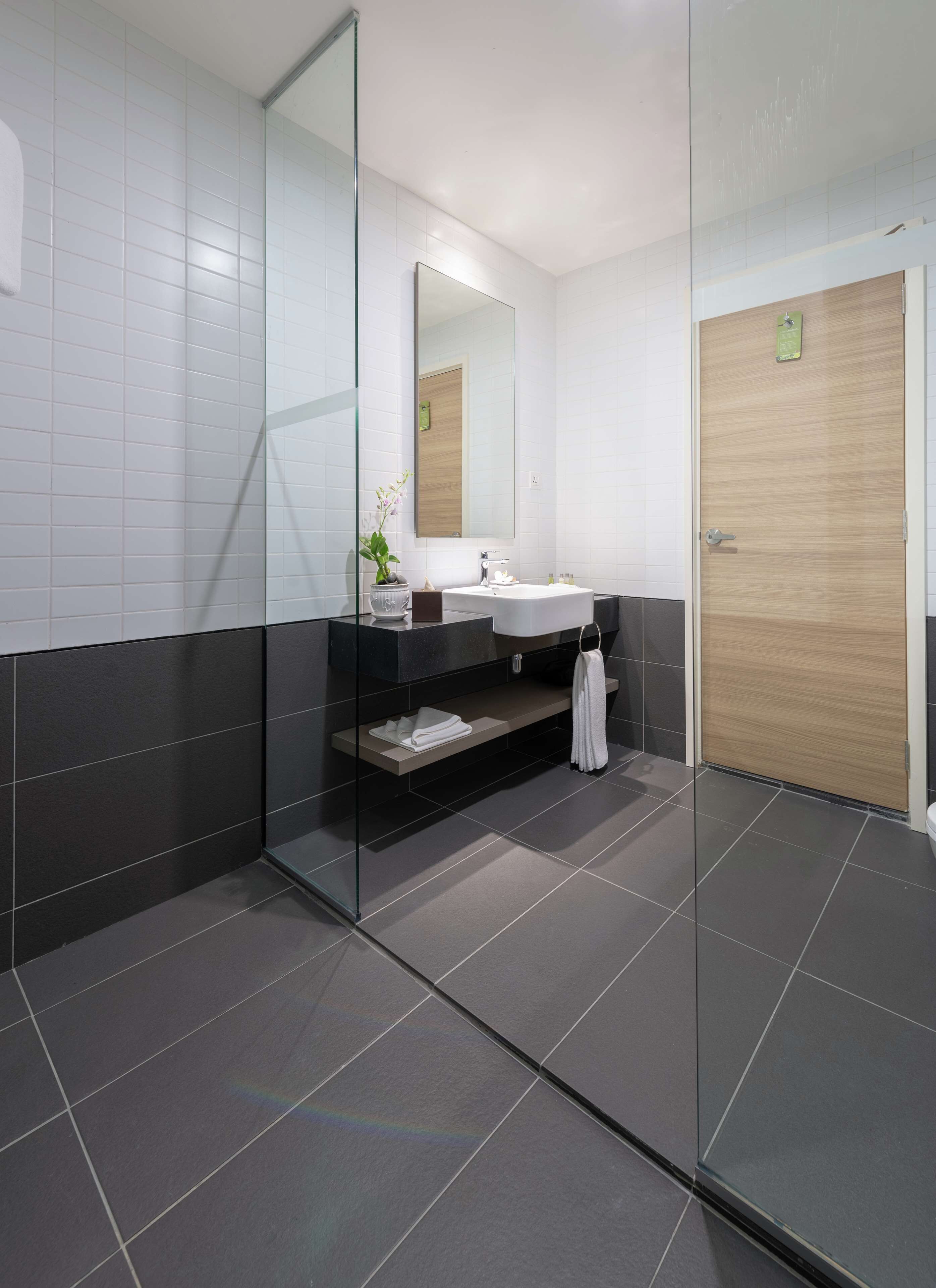 A modern bathroom with a glass shower enclosure, a white sink, and a wooden door.