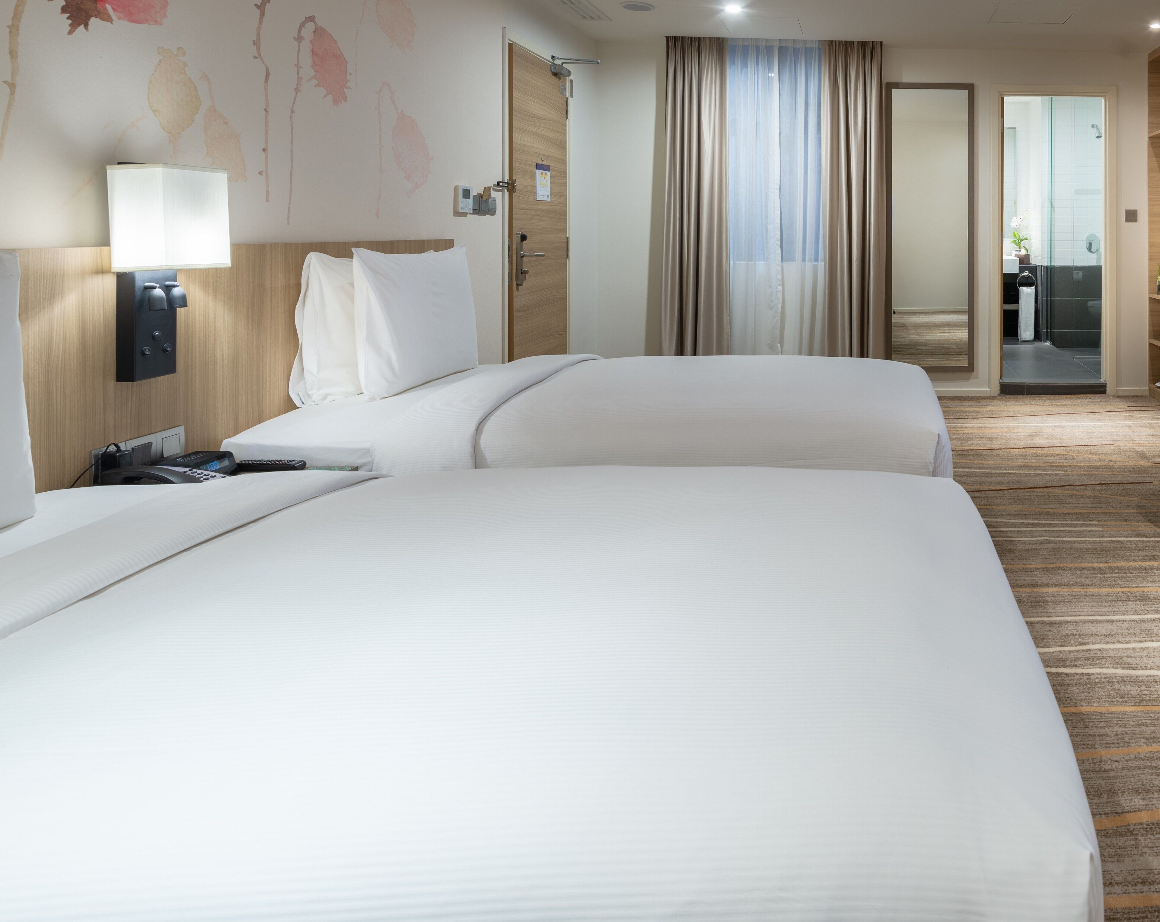 Una habitación de hotel con una cama grande, una mesita de noche con lámpara, un teléfono y un panel de control en la pared.