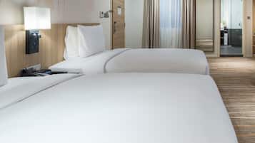 Una habitación de hotel con una cama grande, una mesita de noche con lámpara, un teléfono y un panel de control en la pared.