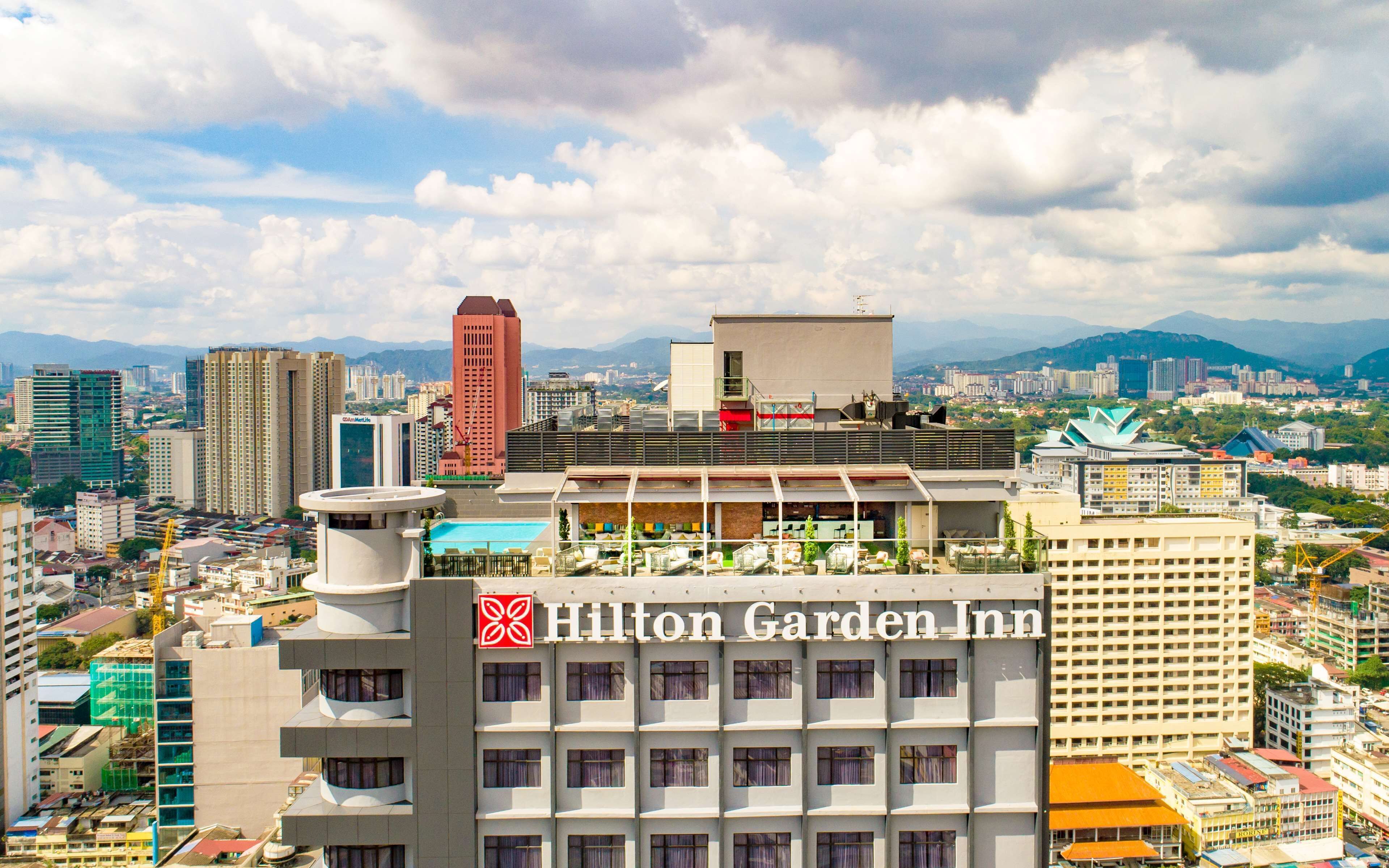 Edifício do Hilton Garden Inn com piscina no terraço e vista para o horizonte urbano.