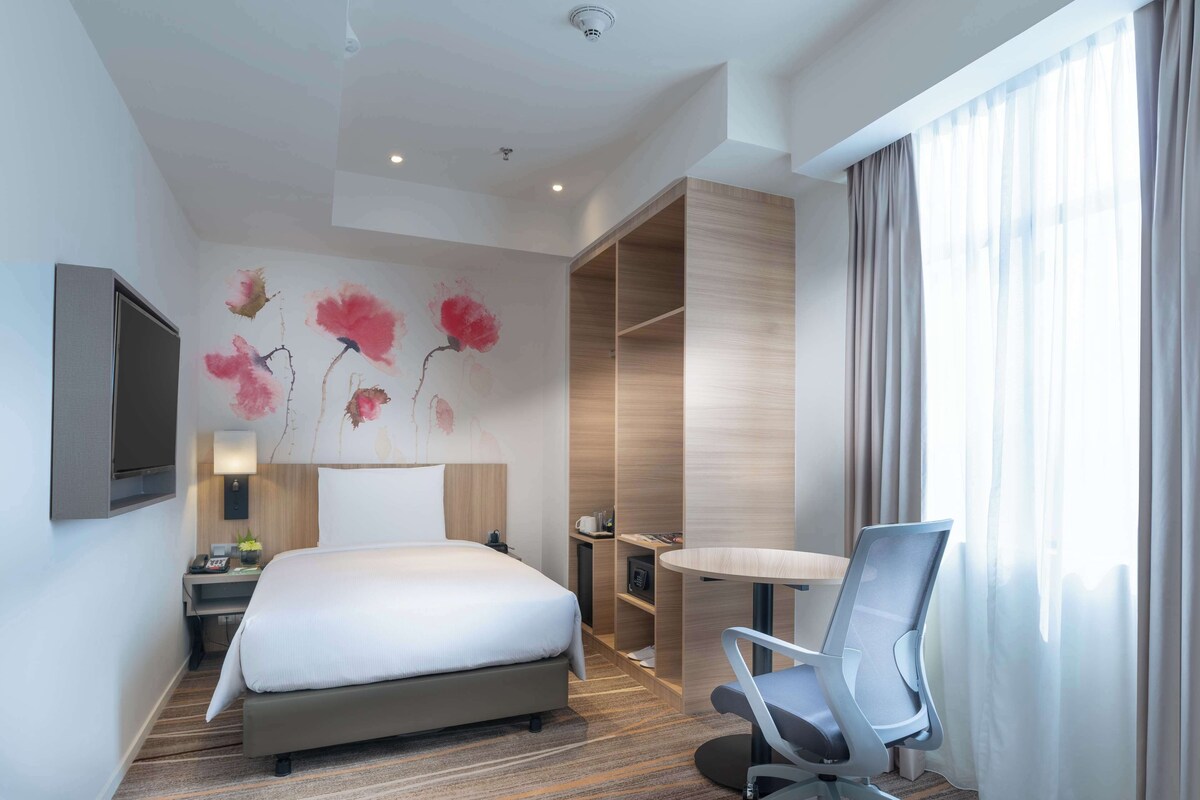 Ein Hotelzimmer mit Bett, Schreibtisch, Stuhl, Fernseher und einem Bild an der Wand.