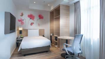 A hotel room with a bed, a desk, a chair, a TV, and a painting on the wall.