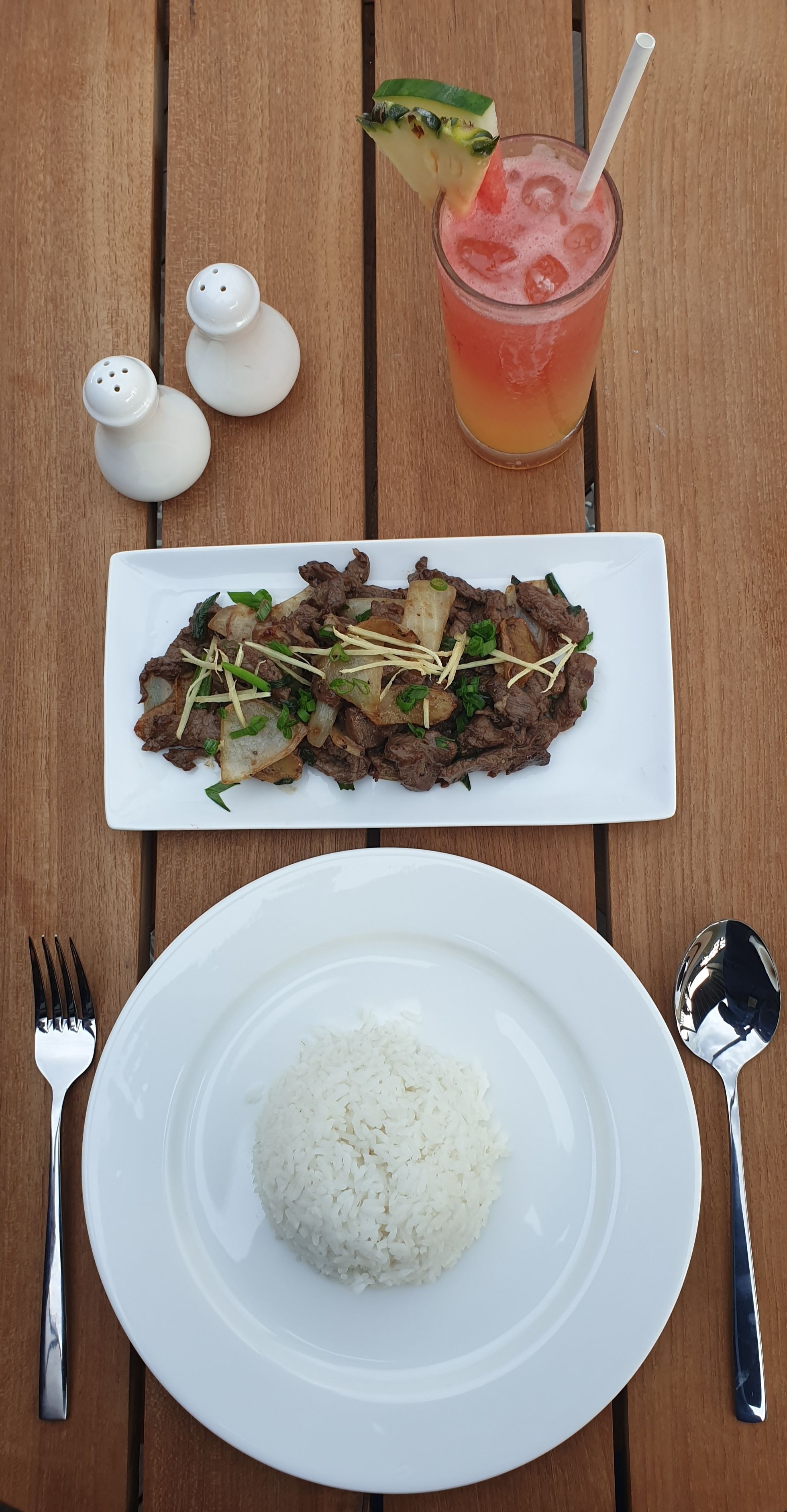 Un repas composé de bœuf sauté, de riz et d’une boisson tropicale, servi sur une table en bois.