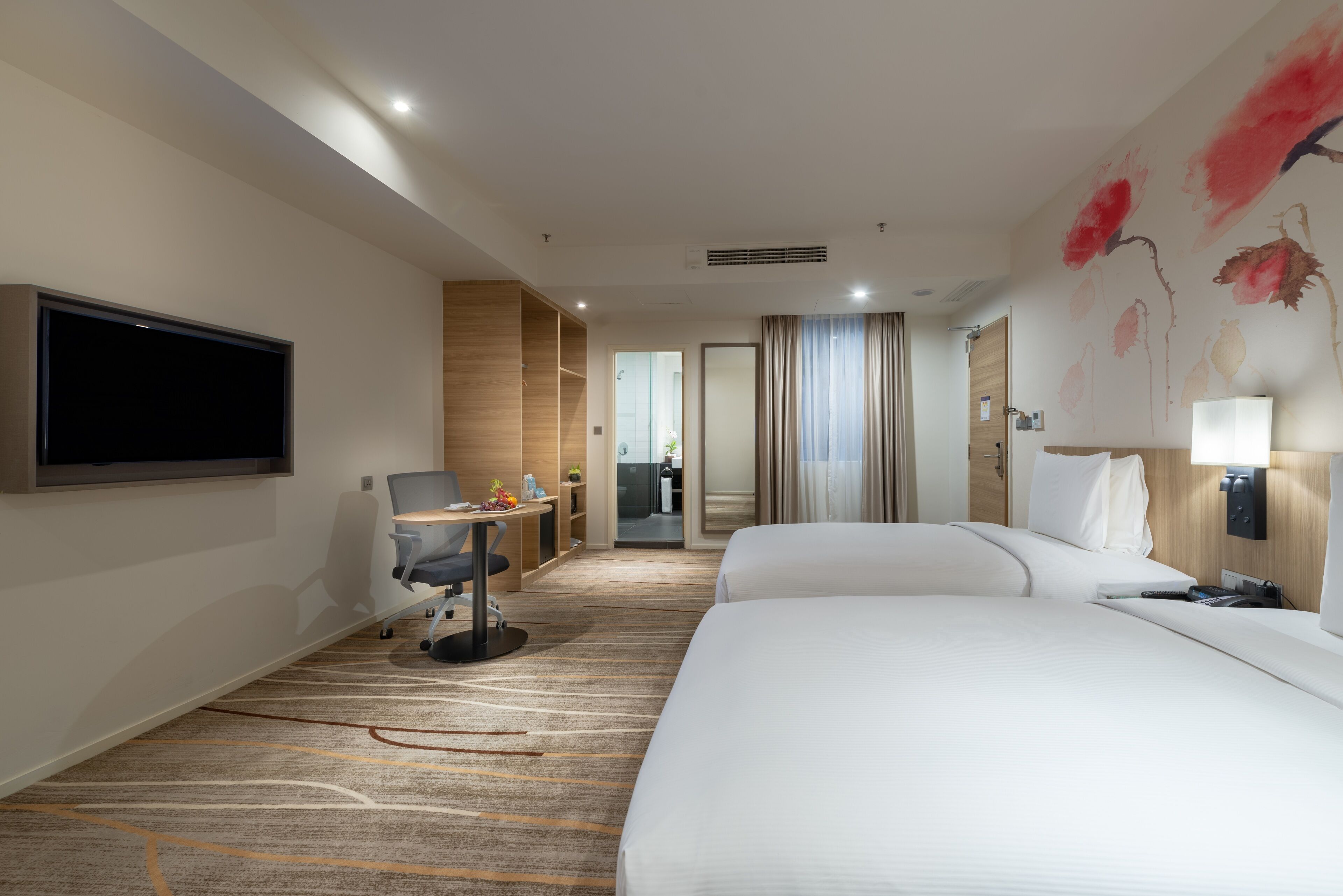 A hotel room with two beds, a desk, a chair, a TV, and a bathroom visible through an open door.