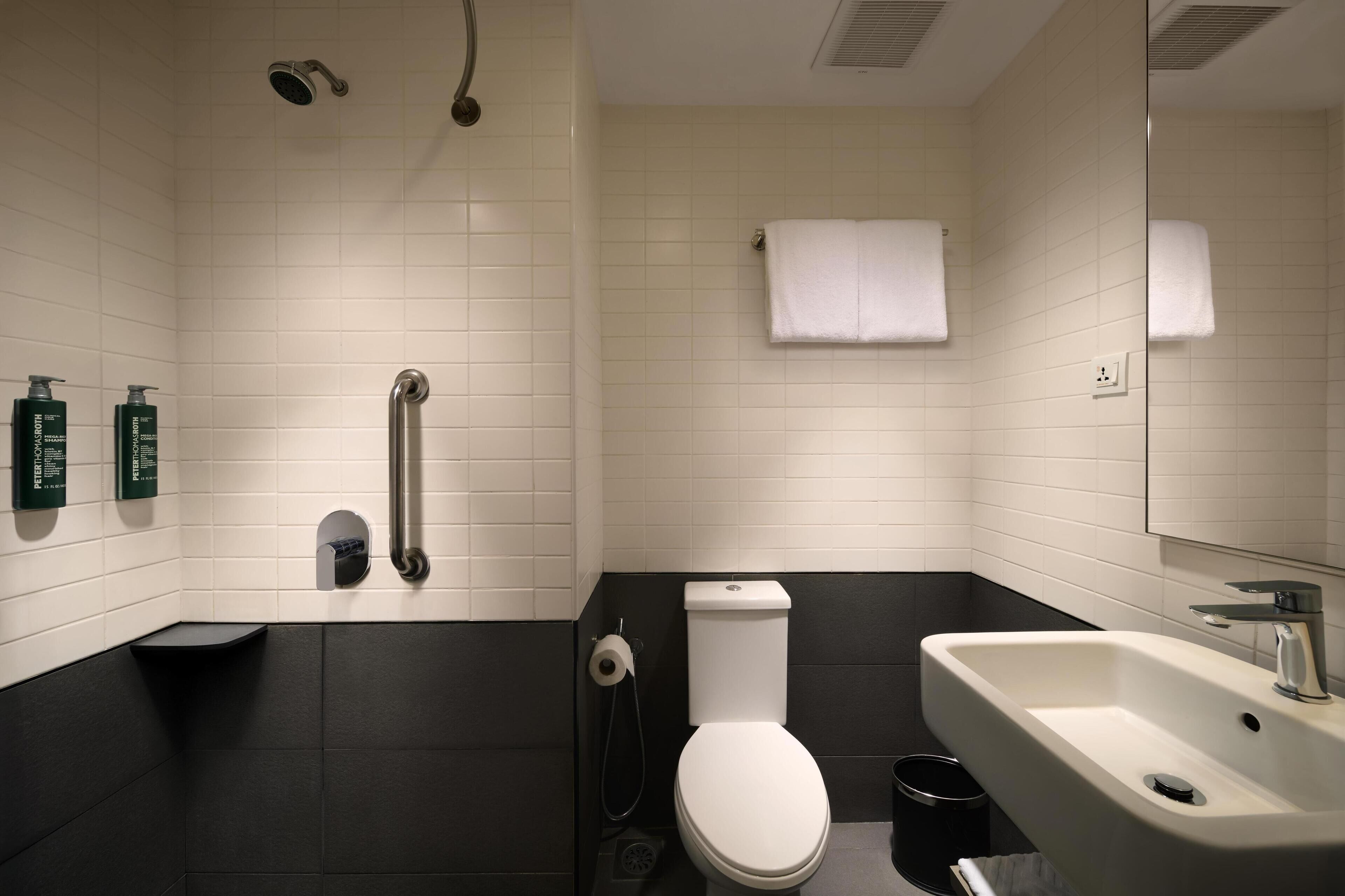A modern bathroom with a white toilet, a black bathtub, a white sink, and a shower.