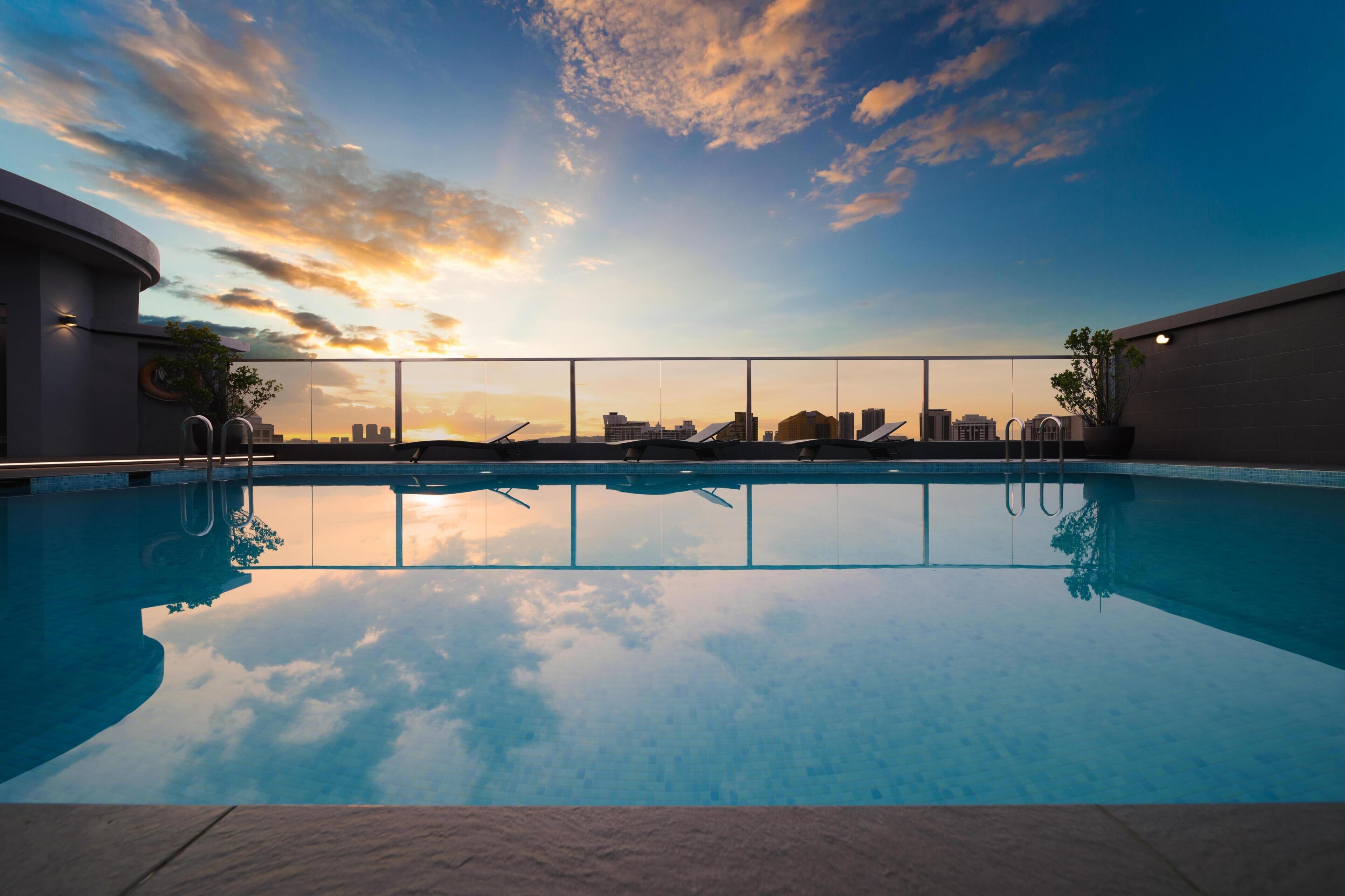 A rooftop pool with a city skyline view at sunset.