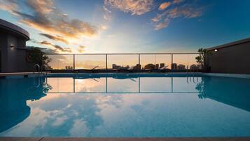 Una piscina en la azotea con vista al horizonte de la ciudad al atardecer.