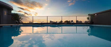 A rooftop pool with a city skyline view at sunset.