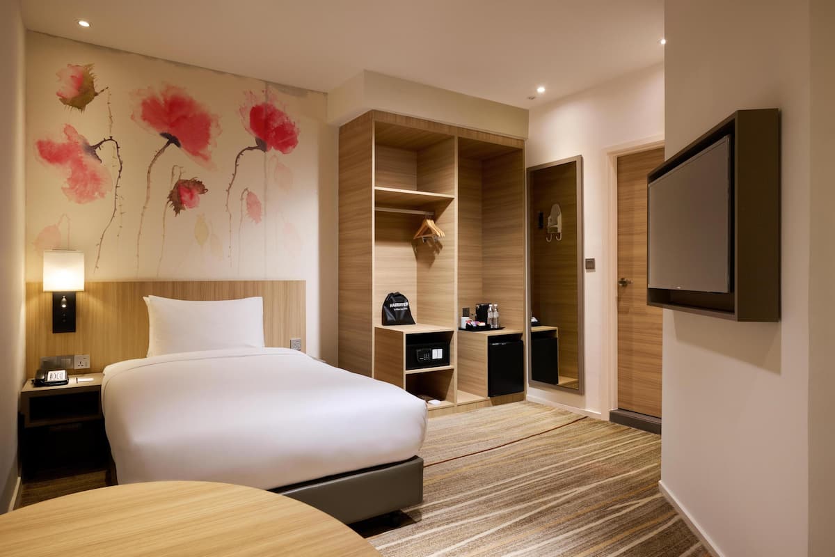 A hotel room with a large bed, a wooden wardrobe, a TV mounted on the wall, and a painting on the wall.