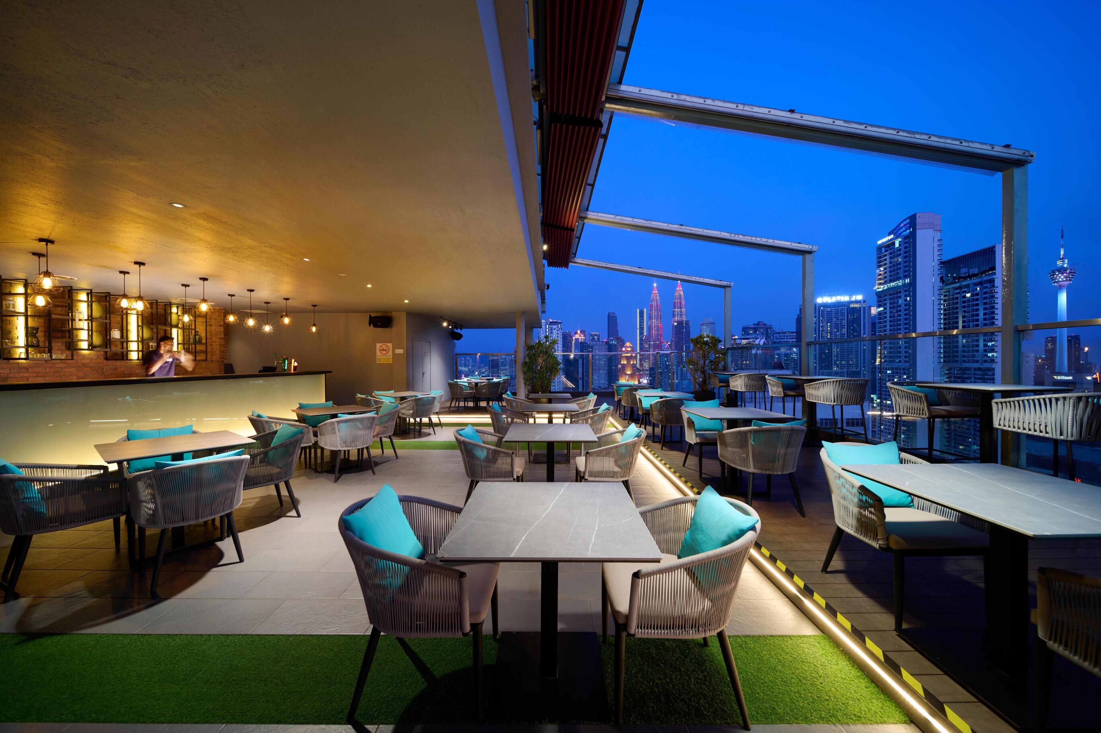 Een terras met tafels en stoelen, een bar en een stadszicht op de achtergrond.