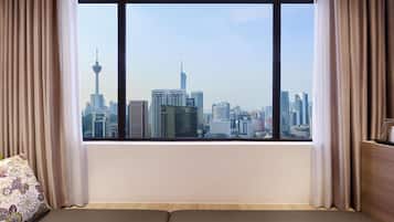 A room with a large window offering a cityscape view, a sofa, and curtains.