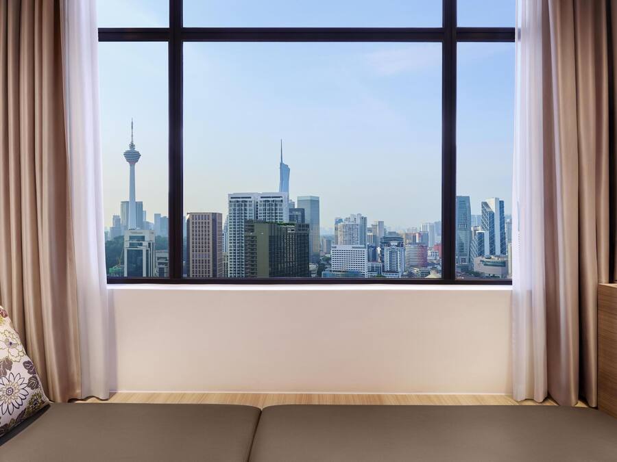 A room with a large window offering a cityscape view, a sofa, and curtains.