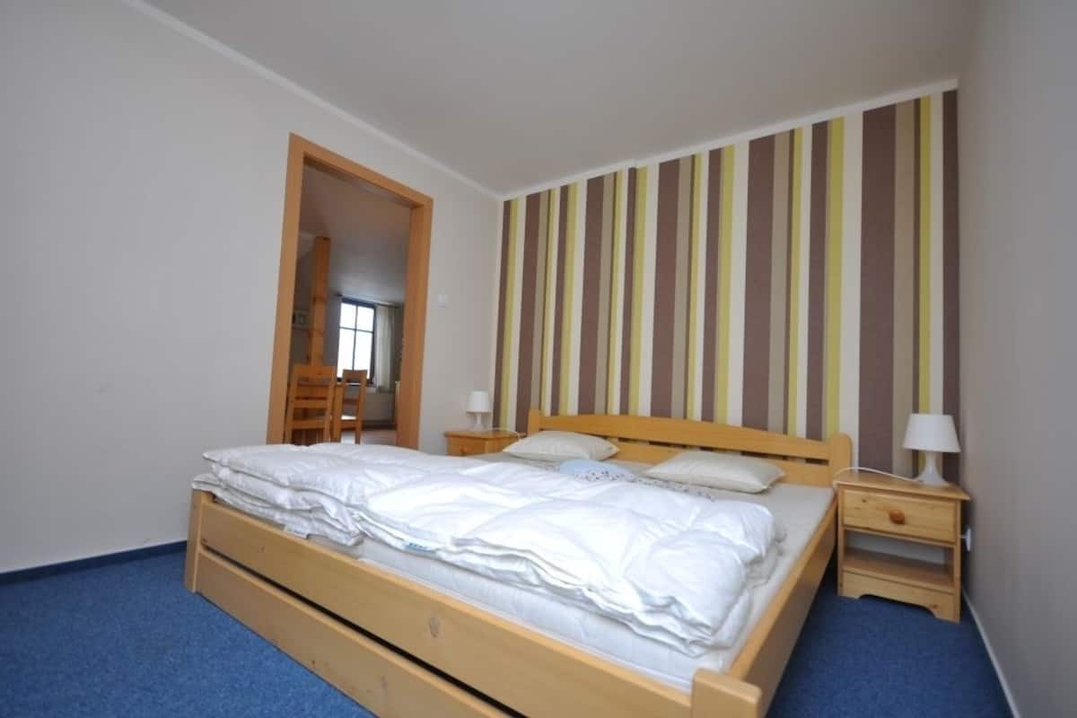 Een eenpersoonskamer met een houten bedframe, wit beddengoed, een gestreepte wand en een klein nachtkastje met een lamp.