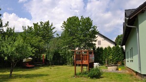 A wooden play structure in a grassy yard with a house in the background. - Apartmány Pod Zálesím (Loucna nad Desnou)