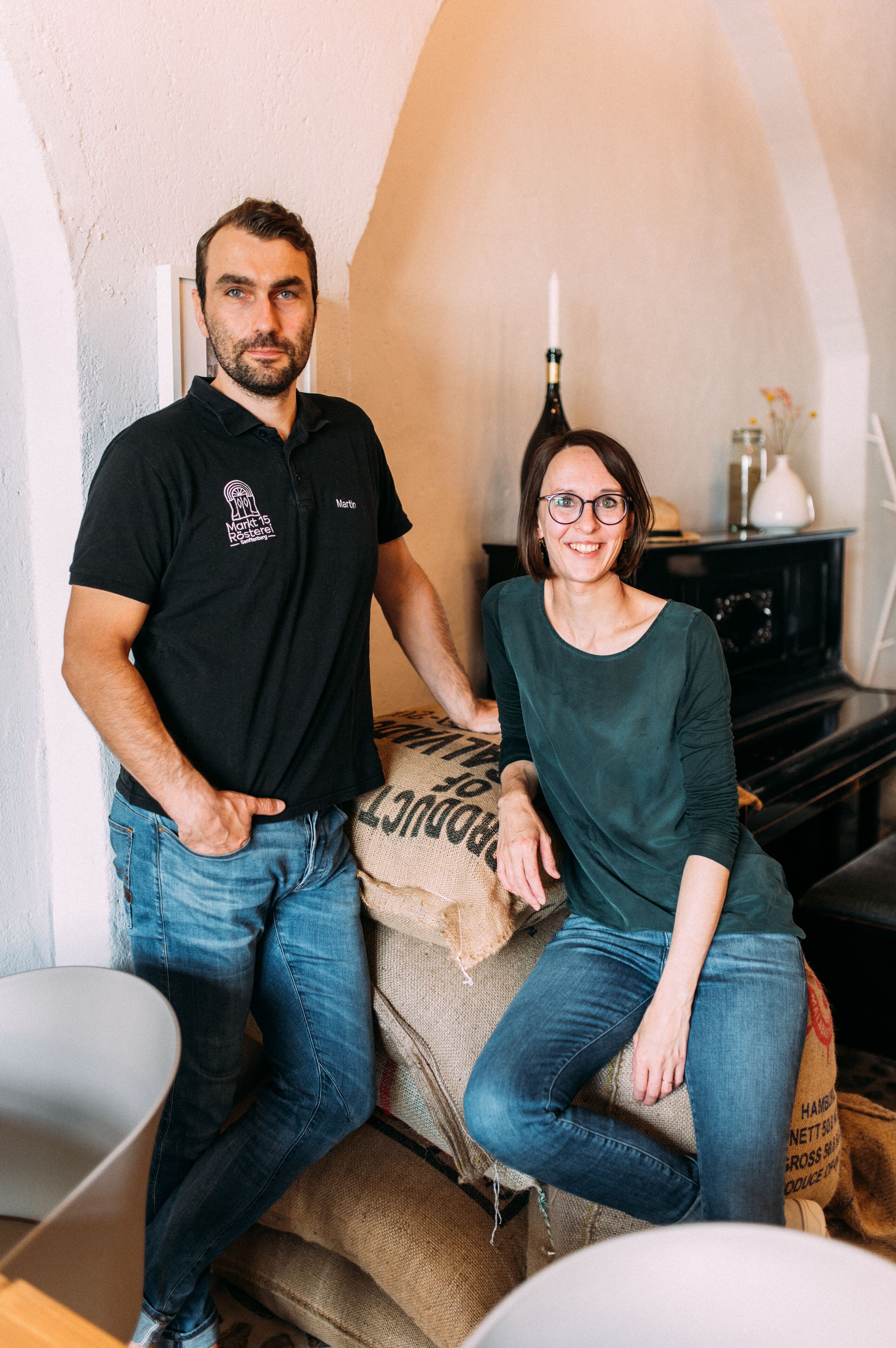 A man and a woman sitting on a couch in a room with a white wall and a wooden cabinet in the background.