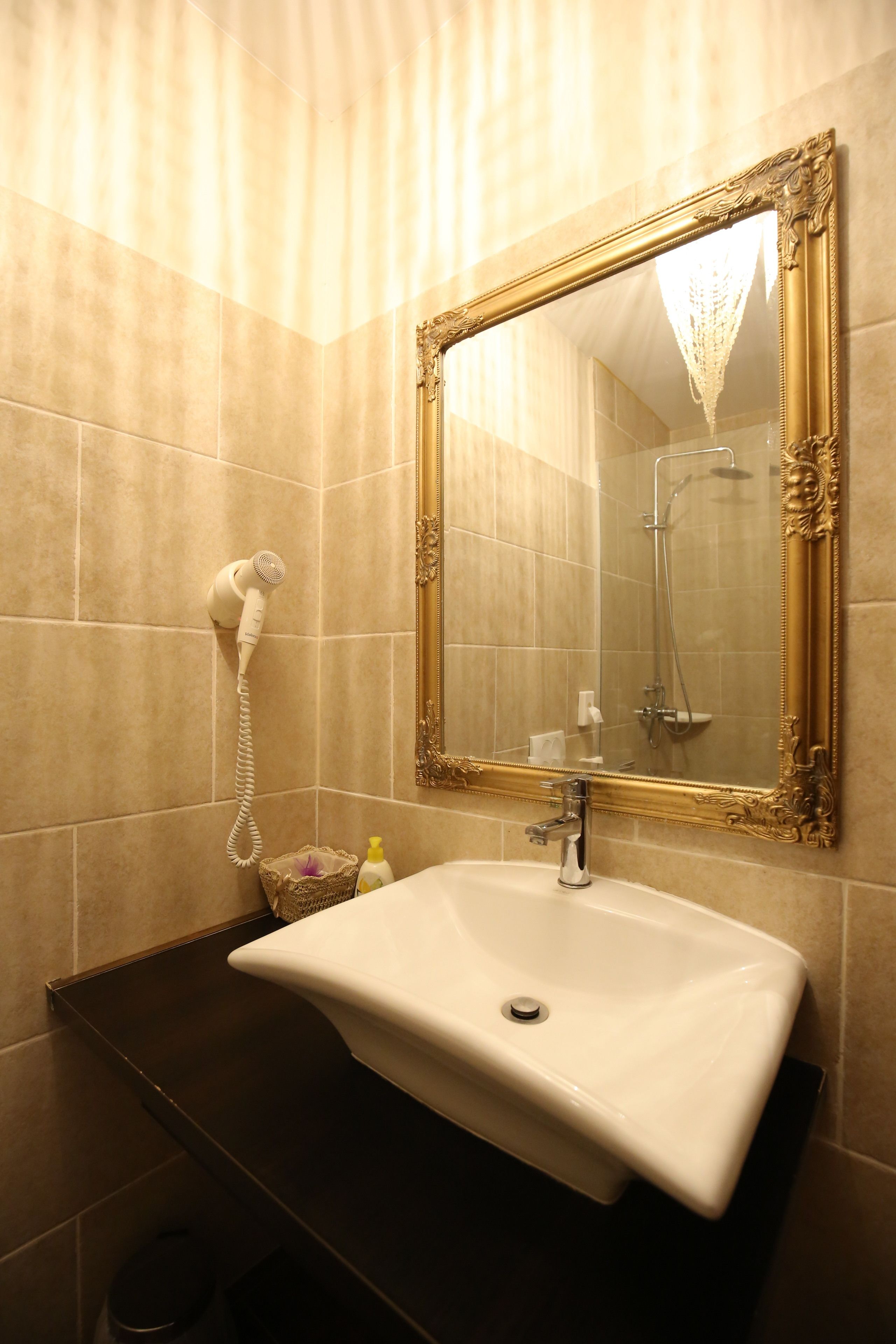 Een badkamer met een wit wastafelmeubel, een spiegel met gouden lijst en een föhn aan de muur.