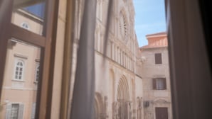 A view through a window of a building with a large arched doorway and a clock tower. - Luxury Rooms Contessa Vitali (Zadar)