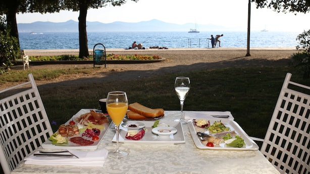 A table set with food and drinks overlooking a beach with people in the background. - Luxury Rooms Contessa Vitali (Zadar)