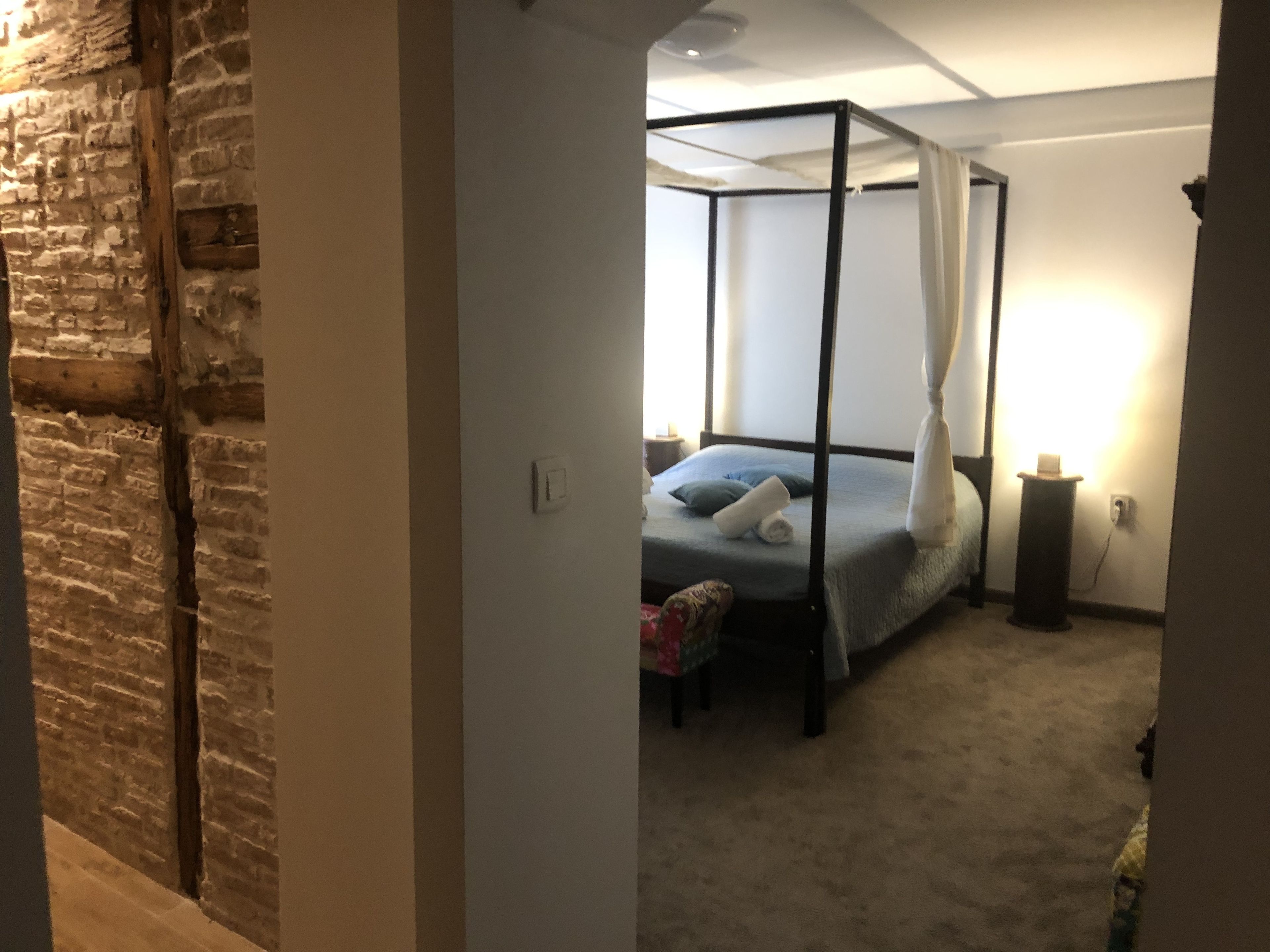 Une chambre à coucher avec un lit à baldaquin, une table de chevet, une lampe et un mur en briques.