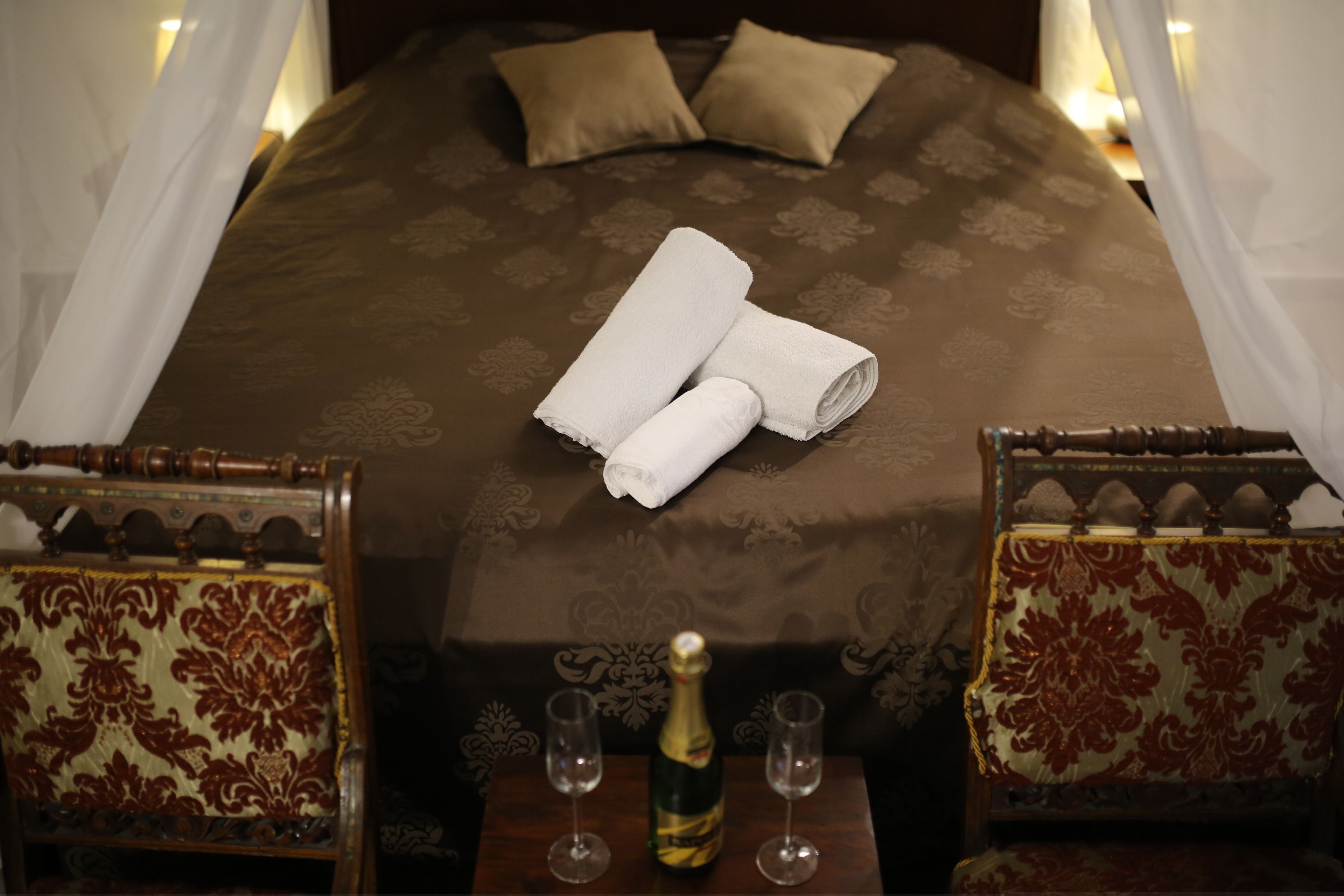Ein ordentlich bezogenes Bett mit zwei Kissen, eine Champagnerflasche und zwei leere Gläser auf einem Holztisch.