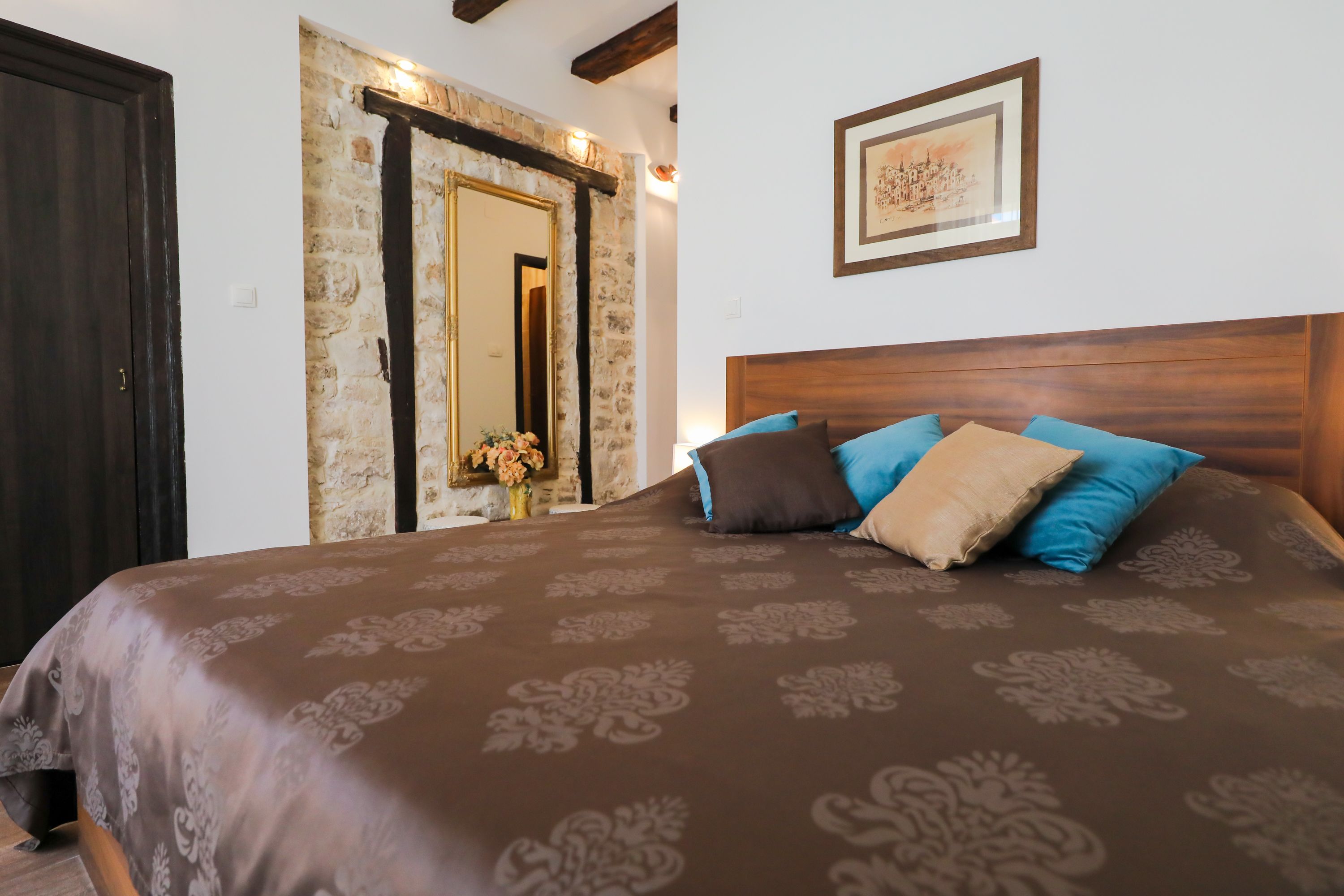 A bedroom with a large bed, a wooden headboard, a stone wall, and a framed picture on the wall.