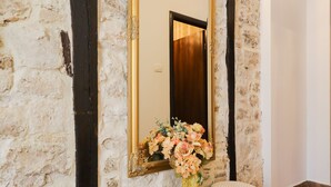 A room with a stone wall, a large mirror, two stools, and a vase with flowers. - Luxury Rooms Contessa Vitali (Zadar)