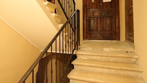 A staircase with a wooden handrail and a dark metal railing, leading to a wooden door with a plaque. - Luxury Rooms Contessa Vitali (Zadar)